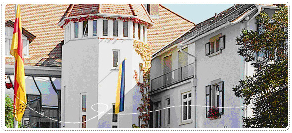 オレンジ色の三角屋根で白い壁、窓からドイツの旗が下がっている建物の写真