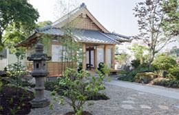 日本式建築の建物と石灯篭、庭に植えられた植木の写真