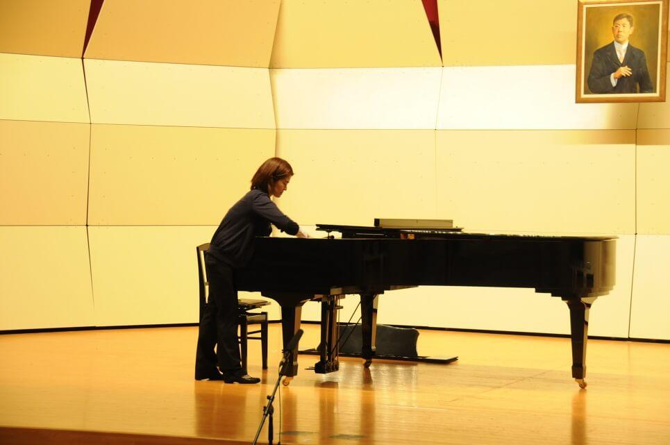 舞台にあるピアノの調律をしている財津さんの写真