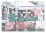 緑色のジャージを着た女の子3人が染め物作品を持って写っている記念写真