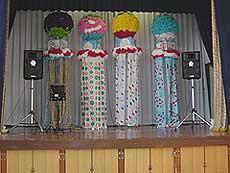 舞台の上に大きなくす玉の下に吹き流しの付いた綺麗な七夕飾りが4個展示してあり、両脇にスタンド付きのスピーカーが置かれている写真