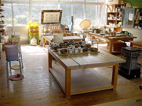 室内に木製の机が4台置かれ、机の上には同芸の作品が置かれており、陶芸に必要な機材が置かれている陶芸作業室の写真