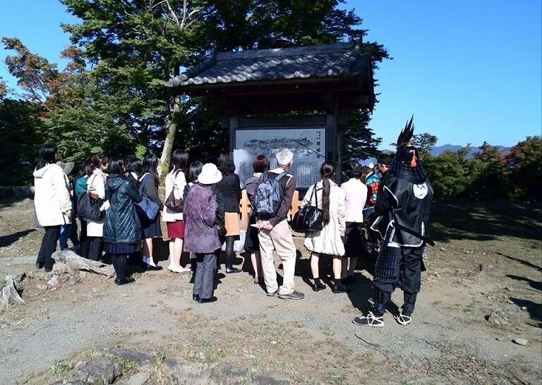 説明看板の前でツアーガイドの説明をきいている秋の岡城散策ツアー参加者の写真
