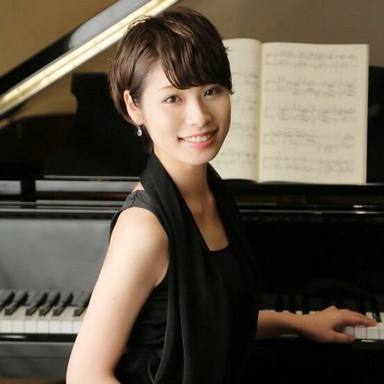 グランドピアノに左手をかけ、黒いドレスを着た小町美佳さんの写真