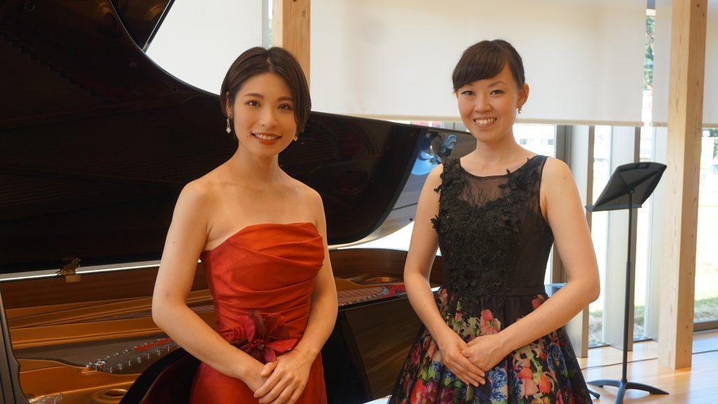 グランドピアノの前で、にこやかにほほ笑む赤いドレスを着た小町さんと黒いドレスを着た田島さんの写真